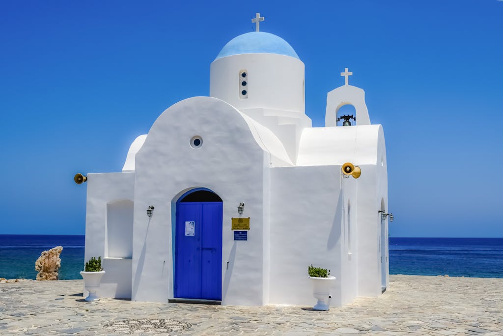 A beautiful white and blue orthodox chapel by the ocean on a sunny day.