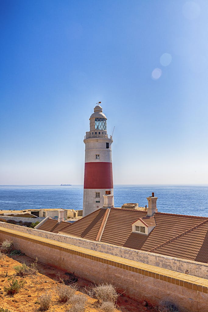 A picturesque lighthouse stands tall by the ocean, surrounded by a serene coastal landscape under a clear blue sky.