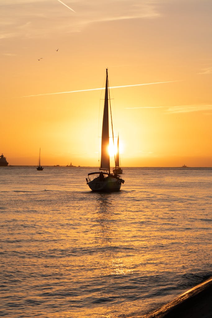 A serene sailboat silhouette at sunset on Lisbon's waters with vibrant sky.